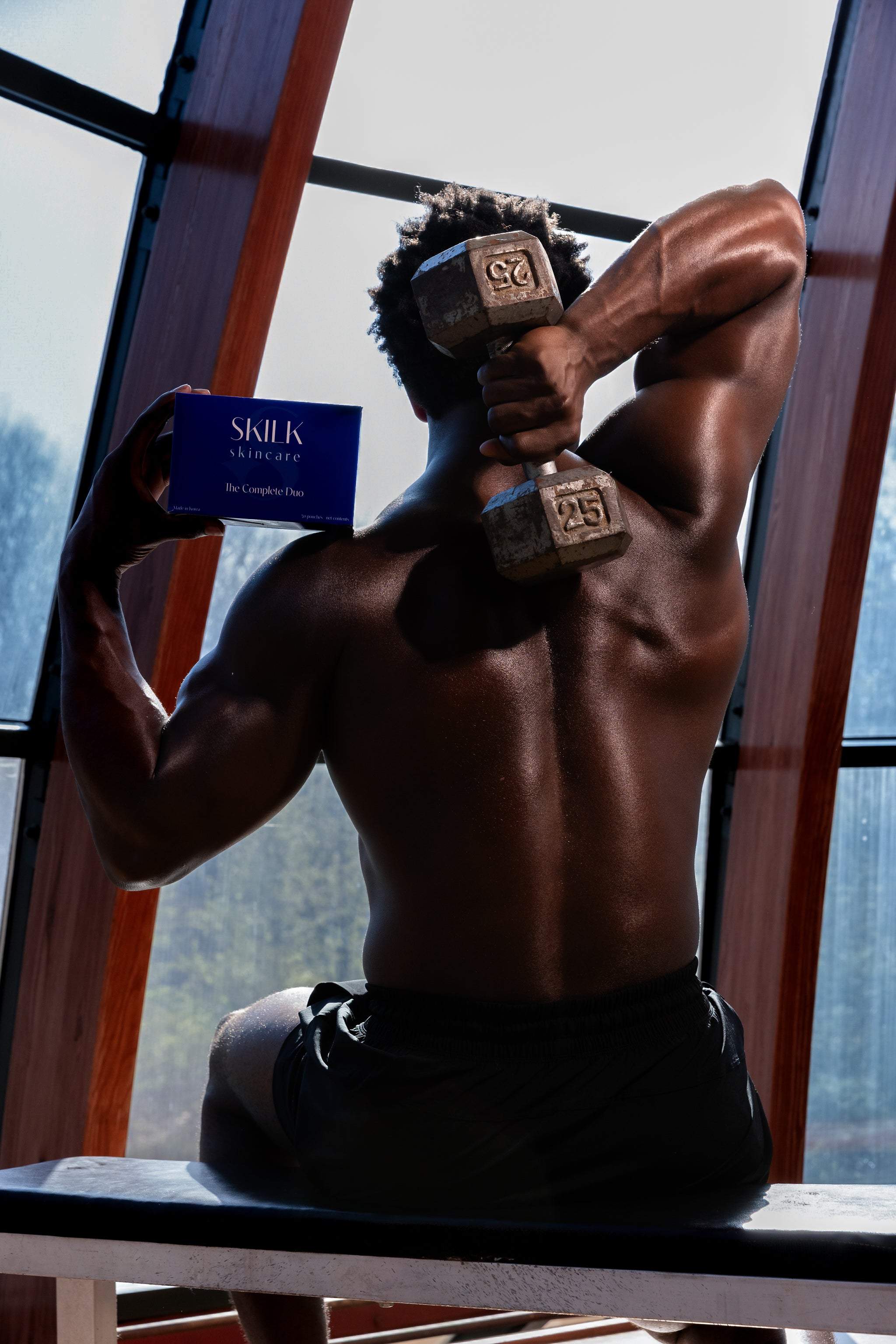 Muscular man lifting weights and holding a Skilk Skin box.