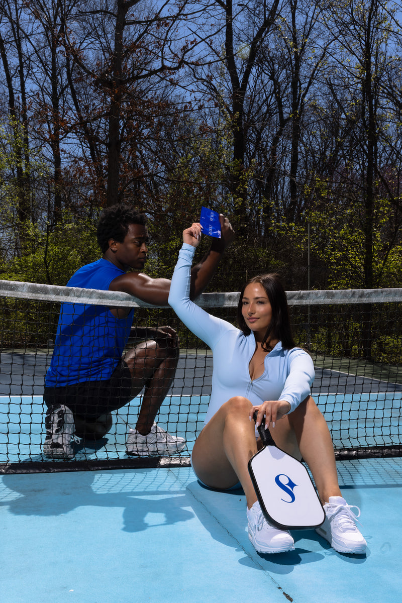 Man handing woman a skilk skin wipe on a pickle ball court